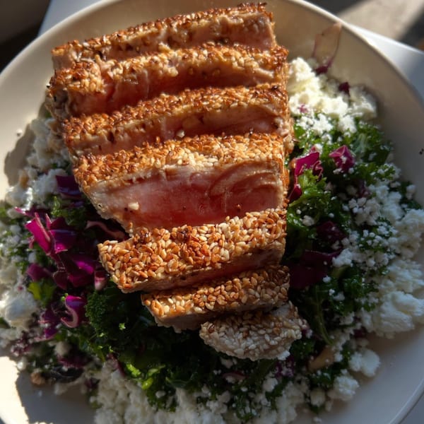 Seared sesame-crusted tuna slices atop a fresh salad with crumbled feta and purple cabbage.