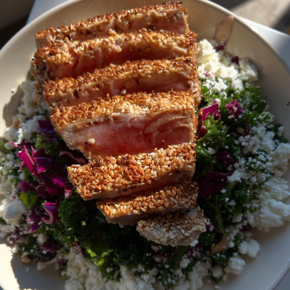 Seared sesame-crusted tuna slices atop a fresh salad with crumbled feta and purple cabbage.