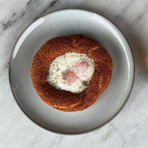 Fora Cafe's simit, a sesame-crusted bread ring, with two baked eggs and pepper on a gray plate.