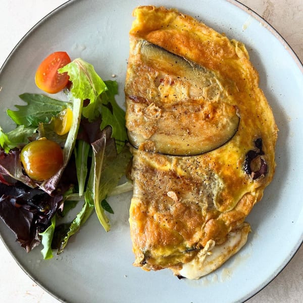 A golden omelet with eggplant and olives, served with a side salad of mixed greens and cherry tomatoes.